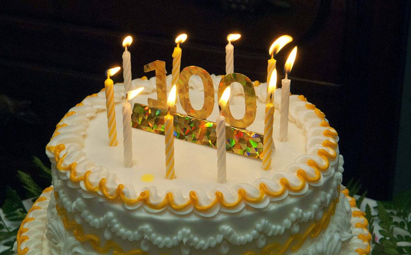 Eine Geburtstagstorte mit Kerzen und der Zahl 100 darauf.