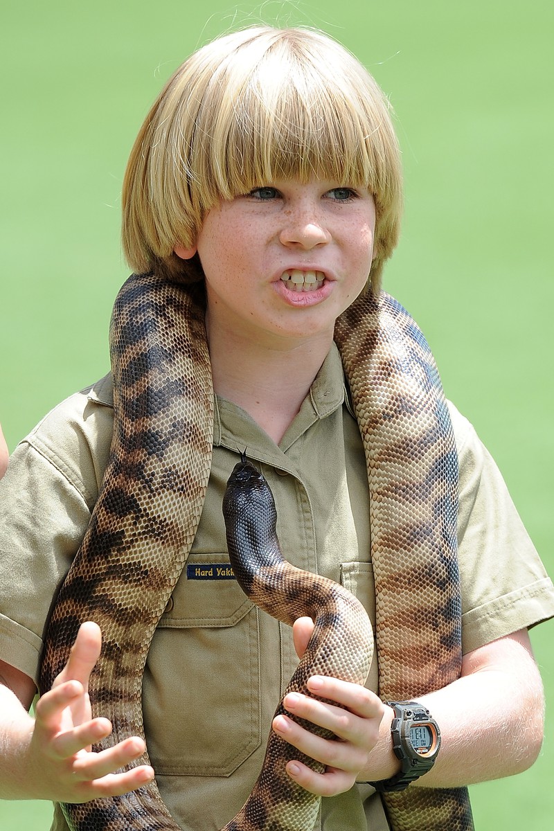 Zu sehen ist Robert Irwin mit einer Schlange, der wie sein Vater Steve Irwin ein Krokodil fütterte.