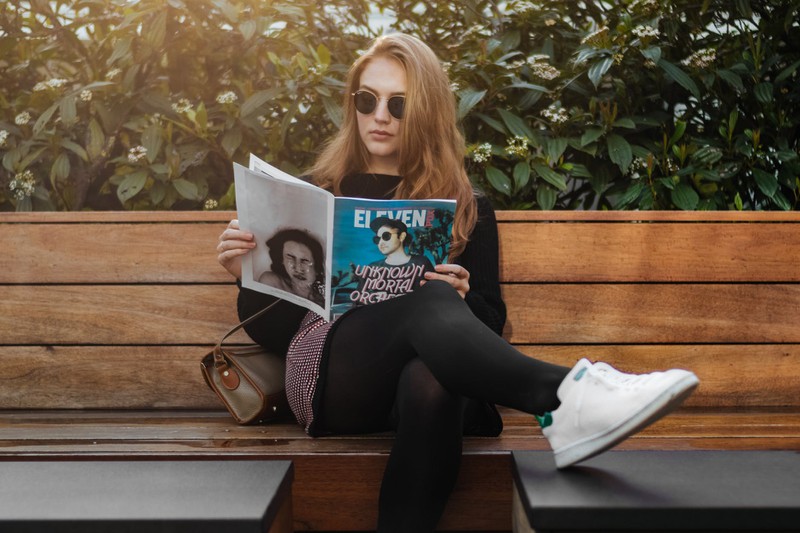Teenagerin, die eine Sonnenbrille trägt und ein Szene-Magazin liest